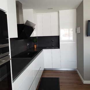 Новый формат декора квартиры: маленькая угловая кухня в стиле модернизм с обеденным столом, врезной раковиной, плоскими фасадами, белыми фасадами, столешницей из цинка, белым фартуком, фартуком из травертина, техникой из нержавеющей стали, темным паркетным полом, коричневым полом и серой столешницей без острова