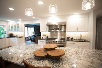 Example of a large classic l-shaped light wood floor, brown floor and tray ceiling eat-in kitchen design in Other with an undermount sink, shaker cabinets, white cabinets, granite countertops, white backsplash, ceramic backsplash, stainless steel appliances, an island and gray countertops