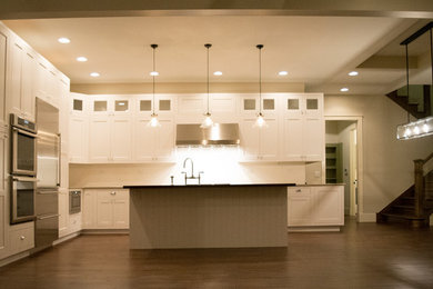 Large minimalist l-shaped medium tone wood floor eat-in kitchen photo in Chicago with a farmhouse sink, shaker cabinets, white cabinets, quartz countertops, white backsplash, subway tile backsplash, stainless steel appliances and an island