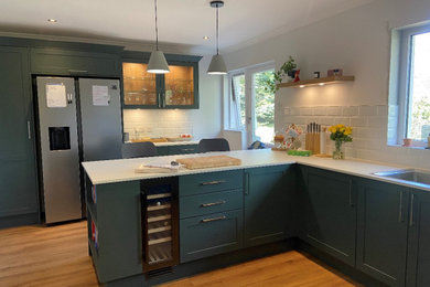 Mid-sized modern u-shaped open plan kitchen in Edinburgh with a single-bowl sink, shaker cabinets, green cabinets, white splashback, panelled appliances, a peninsula, beige floor and white benchtop.