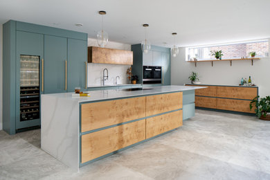 Inspiration for an expansive contemporary l-shaped open plan kitchen in Devon with a built-in sink, flat-panel cabinets, blue cabinets, engineered stone countertops, grey splashback, engineered quartz splashback, stainless steel appliances, limestone flooring, an island, grey floors and grey worktops.