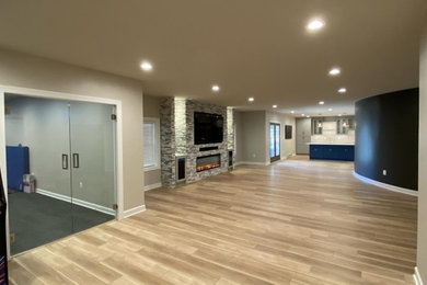 This is an example of a large contemporary walk-out basement in Baltimore with a game room, beige walls, vinyl floors, a hanging fireplace and multi-coloured floor.