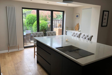 Medium sized contemporary grey and white galley kitchen/diner in Other with an integrated sink, flat-panel cabinets, blue cabinets, quartz worktops, grey splashback, engineered quartz splashback, black appliances, laminate floors, a breakfast bar, brown floors, grey worktops, a drop ceiling and feature lighting.