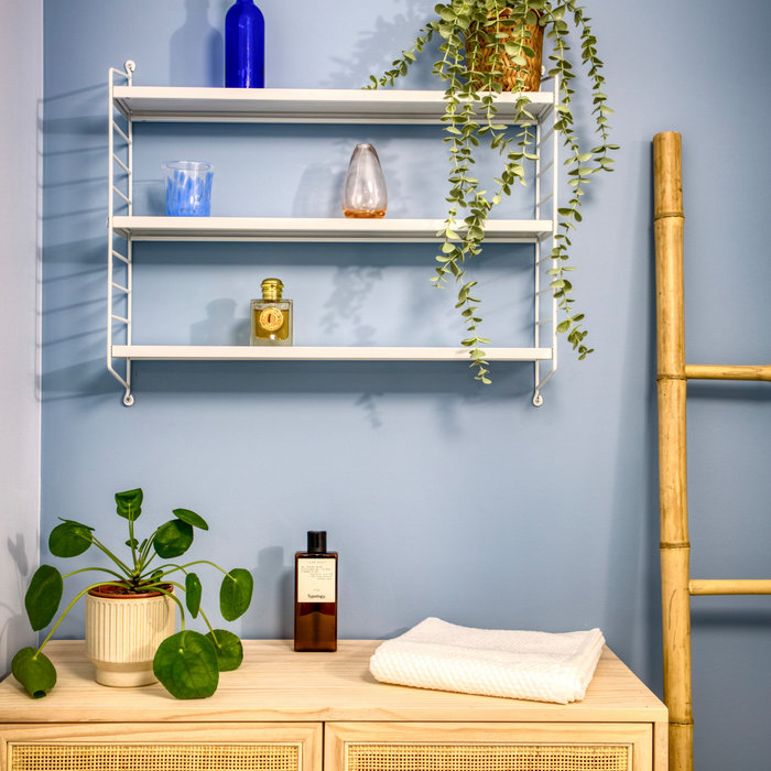 Cette salle de bain toute blanche s'est parée de 2 nuances de bleu, au mur et de meubles naturels surmontée d'une étagère blanche.