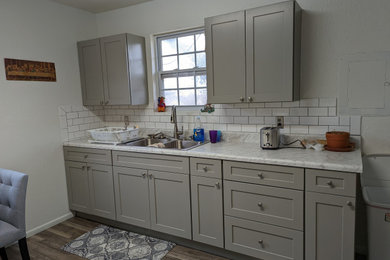 Ejemplo de cocina tradicional de tamaño medio con puertas de armario grises, encimera de laminado, salpicadero blanco, salpicadero de azulejos tipo metro y suelo vinílico