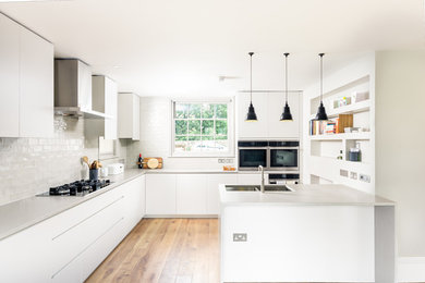 This is an example of a mid-sized contemporary u-shaped separate kitchen in Sussex with a drop-in sink, flat-panel cabinets, grey cabinets, quartz benchtops, grey splashback, cement tile splashback, stainless steel appliances, light hardwood floors, with island and brown floor.