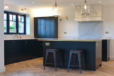 This is an example of a large contemporary u-shaped open plan kitchen in Kent with a double-bowl sink, shaker cabinets, green cabinets, marble benchtops, white splashback, marble splashback, coloured appliances, laminate floors, with island, brown floor and white benchtop.