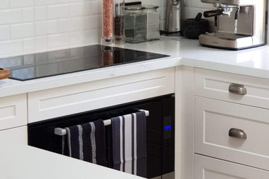 Photo of a large traditional u-shaped kitchen pantry in Gold Coast - Tweed with a farmhouse sink, shaker cabinets, white cabinets, quartz benchtops, white splashback, subway tile splashback, black appliances, ceramic floors, multi-coloured floor and white benchtop.