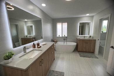 Inspiration for a modern master gray tile and ceramic tile double-sink freestanding bathtub remodel in Other with flat-panel cabinets, medium tone wood cabinets, quartz countertops, gray countertops and a one-piece toilet
