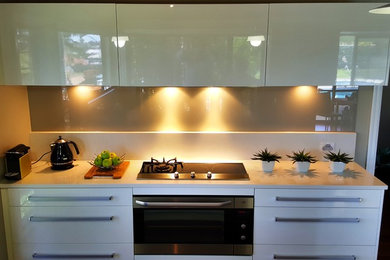 Inspiration for a contemporary single-wall open plan kitchen in Brisbane with a double-bowl sink, flat-panel cabinets, white cabinets, a peninsula, glass sheet splashback, stainless steel appliances and medium hardwood floors.