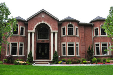 Inspiration for a large timeless red two-story brick exterior home remodel in New York with a hip roof