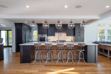 Open concept kitchen - transitional medium tone wood floor and brown floor open concept kitchen idea in New York with a farmhouse sink, shaker cabinets, black cabinets, white backsplash, stone slab backsplash, stainless steel appliances, an island and brown countertops