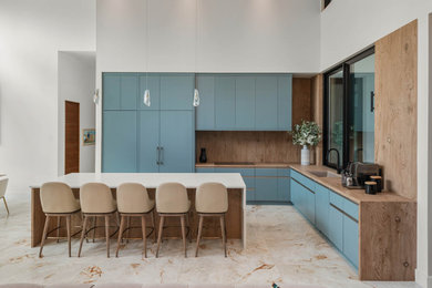 Example of a large trendy l-shaped marble floor and white floor eat-in kitchen design with flat-panel cabinets, wood countertops and an island