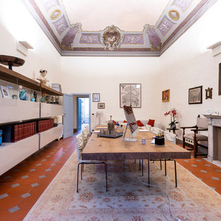 フィレンツェの大きいモダンスタイルのおしゃれな書斎 (白い壁、テラコッタタイルの床、標準型暖炉、コンクリートの暖炉まわり、自立型机、茶色い床) の写真