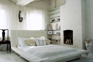 This is an example of a small contemporary master bedroom in London with white walls, light hardwood flooring, a standard fireplace and a brick fireplace surround.