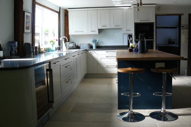 Photo of a large contemporary l-shaped kitchen/diner in Kent with a double-bowl sink, shaker cabinets, grey cabinets, quartz worktops, glass sheet splashback, black appliances, limestone flooring, an island, grey floors and grey worktops.