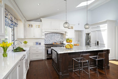 This is an example of a large traditional u-shaped separate kitchen in Phoenix with a farmhouse sink, recessed-panel cabinets, white cabinets, quartz benchtops, white splashback, panelled appliances, medium hardwood floors, with island, ceramic splashback, brown floor and white benchtop.