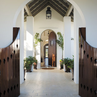 Выдающиеся фото от архитекторов и дизайнеров интерьера: большой вестибюль в средиземноморском стиле с одностворчатой входной дверью, входной дверью из темного дерева, белыми стенами, кирпичным полом и бежевым полом