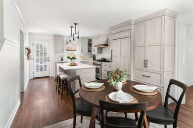 Eat-in kitchen - mid-sized transitional l-shaped medium tone wood floor and brown floor eat-in kitchen idea in New York with a farmhouse sink, shaker cabinets, beige cabinets, quartz countertops, white backsplash, porcelain backsplash, paneled appliances, an island and white countertops