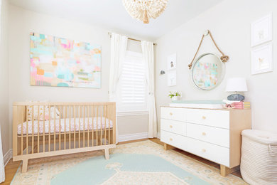 Photo of a small transitional nursery for girls in Los Angeles with beige walls and light hardwood floors.
