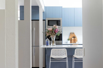 Mid-sized midcentury kitchen pantry in Sydney with a double-bowl sink, blue cabinets, quartz benchtops, white splashback, porcelain splashback, stainless steel appliances, medium hardwood floors and white benchtop.