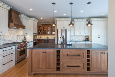 Huge arts and crafts u-shaped medium tone wood floor and brown floor kitchen photo in Other with a farmhouse sink, shaker cabinets, white cabinets, gray backsplash, stainless steel appliances, an island and gray countertops