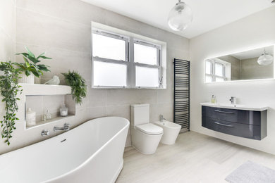 Large contemporary grey and white ensuite bathroom in Sussex with flat-panel cabinets, grey cabinets, a freestanding bath, a walk-in shower, a two-piece toilet, grey tiles, ceramic tiles, white walls, vinyl flooring, a built-in sink, grey floors, an open shower, feature lighting, a single sink and a floating vanity unit.