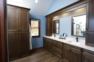 Mid-sized elegant master laminate floor, brown floor and double-sink shower bench photo in Cleveland with raised-panel cabinets, medium tone wood cabinets, a two-piece toilet, blue walls, an undermount sink, a hinged shower door, white countertops and a built-in vanity