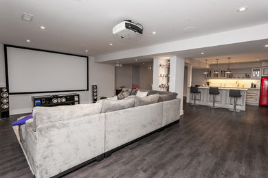 Large contemporary open concept home theatre in Toronto with grey walls, dark hardwood floors, a projector screen and brown floor.