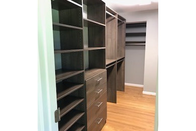 Example of a mid-sized classic gender-neutral light wood floor and brown floor walk-in closet design in Other with flat-panel cabinets and dark wood cabinets