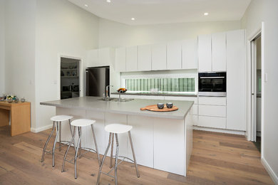 Mid-sized galley kitchen pantry in Sydney with an undermount sink, flat-panel cabinets, white cabinets, quartz benchtops, white splashback, window splashback, stainless steel appliances, light hardwood floors, with island and brown floor.