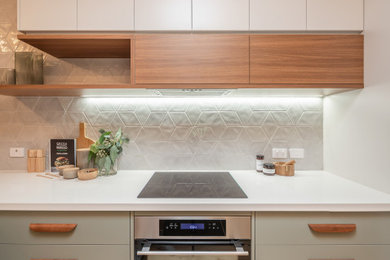 Inspiration for a mid-sized contemporary galley kitchen pantry in Adelaide with an undermount sink, flat-panel cabinets, green cabinets, quartz benchtops, grey splashback, porcelain splashback, stainless steel appliances, light hardwood floors, a peninsula and white benchtop.