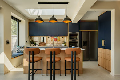 Inspiration for a medium sized scandi galley open plan kitchen in London with a submerged sink, flat-panel cabinets, blue cabinets, composite countertops, multi-coloured splashback, mirror splashback, stainless steel appliances, porcelain flooring, an island, beige floors and white worktops.