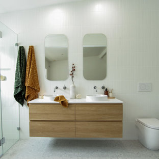 Photo of a mid-sized contemporary 3/4 bathroom in Sydney with medium wood cabinets, a one-piece toilet, white tile, white walls, a vessel sink, grey floor, a hinged shower door, white benchtops, a niche, a double vanity and a floating vanity.