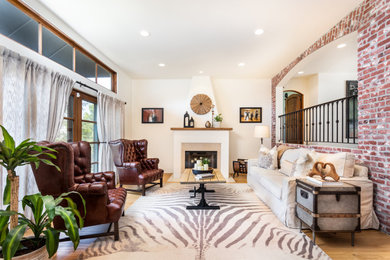 Photo of a mediterranean living room in Los Angeles with white walls, medium hardwood floors, a standard fireplace, brown floor and brick walls.