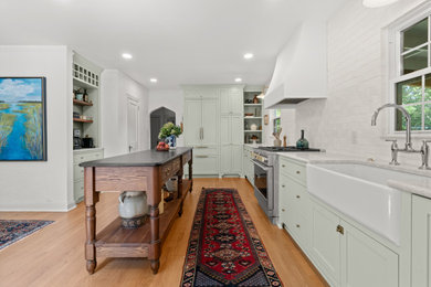 Mid-sized farmhouse galley brown floor kitchen pantry photo in Charleston with a farmhouse sink, shaker cabinets, green cabinets, white backsplash, stainless steel appliances and gray countertops