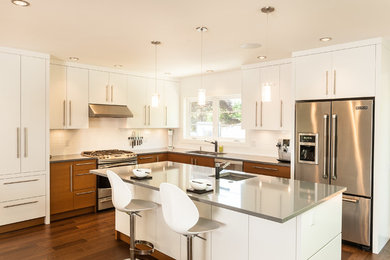 Photo of a contemporary u-shaped eat-in kitchen in Vancouver with a drop-in sink, flat-panel cabinets, white cabinets, laminate benchtops, white splashback, subway tile splashback, stainless steel appliances, dark hardwood floors and with island.