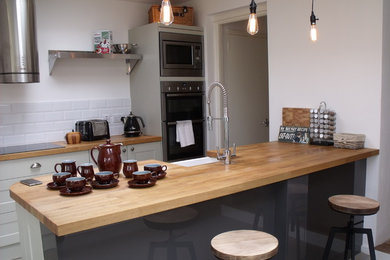 Expansive contemporary u-shaped kitchen/diner in Devon with a submerged sink, louvered cabinets, beige cabinets, wood worktops, white splashback, ceramic splashback, stainless steel appliances, vinyl flooring and a breakfast bar.