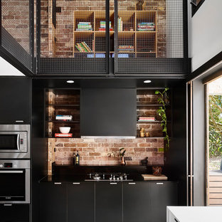 Inspiration pour une grande arrière-cuisine urbaine en L avec un évier encastré, des portes de placard noires, un plan de travail en bois, une crédence en brique, un électroménager en acier inoxydable, béton au sol et un îlot central.