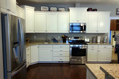 Open concept kitchen - large traditional l-shaped dark wood floor open concept kitchen idea in Salt Lake City with an undermount sink, raised-panel cabinets, white cabinets, granite countertops, beige backsplash, stone slab backsplash, stainless steel appliances and an island