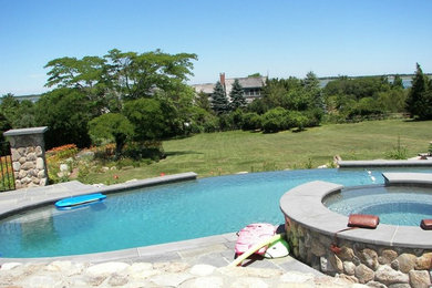 Large mountain style backyard stone and custom-shaped infinity hot tub photo in Boston