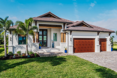 Example of a mid-sized island style white one-story stucco house exterior design in Tampa with a hip roof, a tile roof and a brown roof