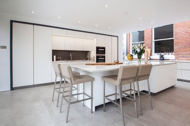 This is an example of a large contemporary l-shaped kitchen in Hampshire with a triple-bowl sink, flat-panel cabinets, white cabinets, grey splashback, stone tile splashback, black appliances, ceramic floors, with island and grey floor.
