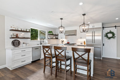 L-shaped light wood floor and brown floor enclosed kitchen photo in San Francisco with a farmhouse sink, raised-panel cabinets, white cabinets, quartz countertops, white backsplash, ceramic backsplash, stainless steel appliances, an island and multicolored countertops