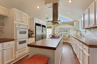 Farmhouse medium tone wood floor kitchen photo in New Orleans with a drop-in sink, shaker cabinets, white cabinets, white backsplash, subway tile backsplash, white appliances and an island