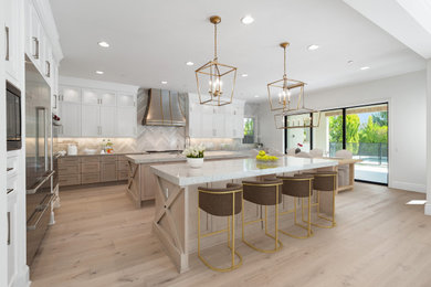 Example of a large trendy l-shaped light wood floor and beige floor open concept kitchen design in Orange County with light wood cabinets, quartz countertops and two islands