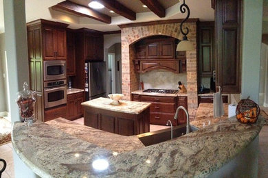 Mid-sized elegant u-shaped ceramic tile open concept kitchen photo in Houston with a farmhouse sink, raised-panel cabinets, dark wood cabinets, granite countertops, beige backsplash, stone tile backsplash, stainless steel appliances and an island
