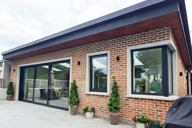 Esempio della facciata di una casa bifamiliare contemporanea a un piano di medie dimensioni con rivestimento in mattoni, tetto a farfalla, copertura in metallo o lamiera e tetto nero
