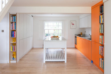 Cette image montre une grande cuisine design en U fermée avec un évier intégré, un placard à porte plane, des portes de placard oranges, un électroménager en acier inoxydable et îlot.