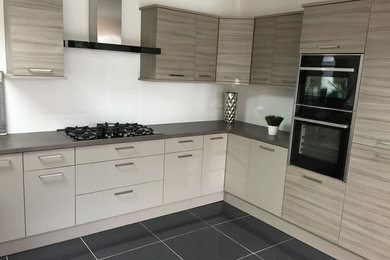 Design ideas for a small contemporary u-shaped kitchen/diner in Oxfordshire with a built-in sink, flat-panel cabinets, light wood cabinets, composite countertops, black appliances, ceramic flooring, a breakfast bar and grey floors.